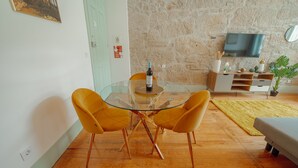 Un salon moderne avec une table à manger en verre, des chaises jaunes, un téléviseur à écran plat et un mur en pierre.