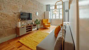 Un salon avec un mur en pierre, un téléviseur à écran plat, un fauteuil jaune, un canapé et une grande fenêtre.