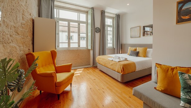 Une chambre d’hôtel moderne dotée d’un grand lit, d’un canapé, d’un fauteuil et offrant une vue sur la ville grâce à de grandes fenêtres.