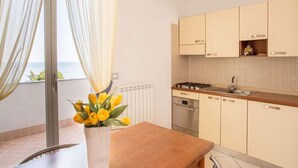 A modern kitchen with a view of the sea, a dining area with a table and chairs, and a window with sheer curtains. - Residence Sant'anna  Two-room Apartment 4 Pax (Pietra Ligure)