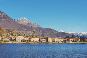 A lakeside town with historic buildings, a prominent tower, and snow-capped mountains in the background.