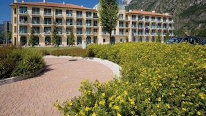 A hotel with multiple balconies, a paved courtyard, and a mountainous backdrop. - Residence Porto Letizia Villas-bilocale 4 Pax Vista Lago Deluxe (Porlezza)