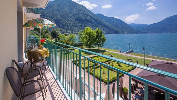 A balcony with a table and chairs, overlooking a lake and mountains.