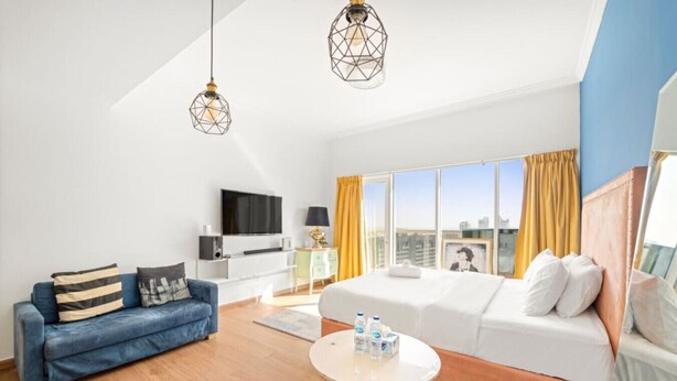 Une chambre d’hôtel moderne avec un canapé, un lit, une télévision, une petite table avec des bouteilles et une vue sur la ville.