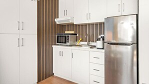 Une cuisine moderne avec des meubles blancs, un réfrigérateur en acier inoxydable, un four à micro-ondes et une bouilloire.