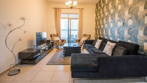 A modern living room with a sofa set, a TV, a decorative floor lamp, and patterned wallpaper.