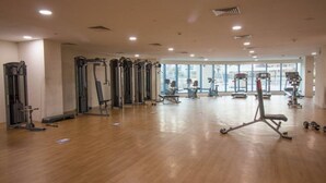 A spacious gym with various exercise equipment, large windows, and a wooden floor.