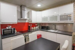 Une cuisine compacte avec des meubles blancs, un plan de travail noir, une hotte en acier inoxydable, un four à micro-ondes, un grille-pain et un évier.