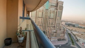 A balcony with a potted plant, a trash bin, and a view of a tall building and roads.