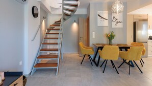 Una cocina moderna con refrigerador empotrado, una zona de comedor con sillas amarillas y una escalera de caracol.