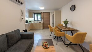Un espacio habitable compacto con sofá, mesa de comedor con sillas, zona de cocina y un reloj en la pared.