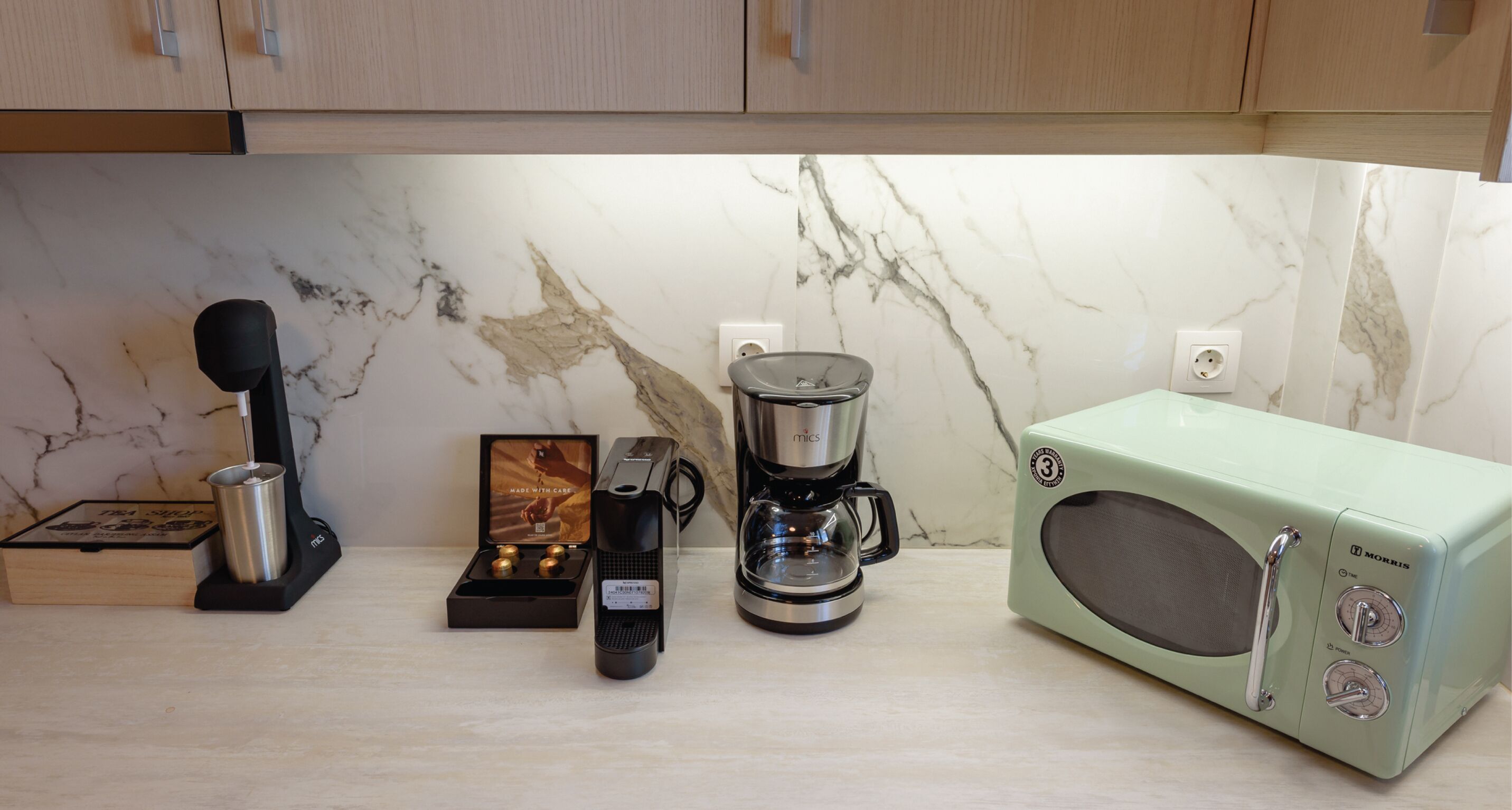 A kitchen with a coffee maker, a microwave, and a tea set on the counter.