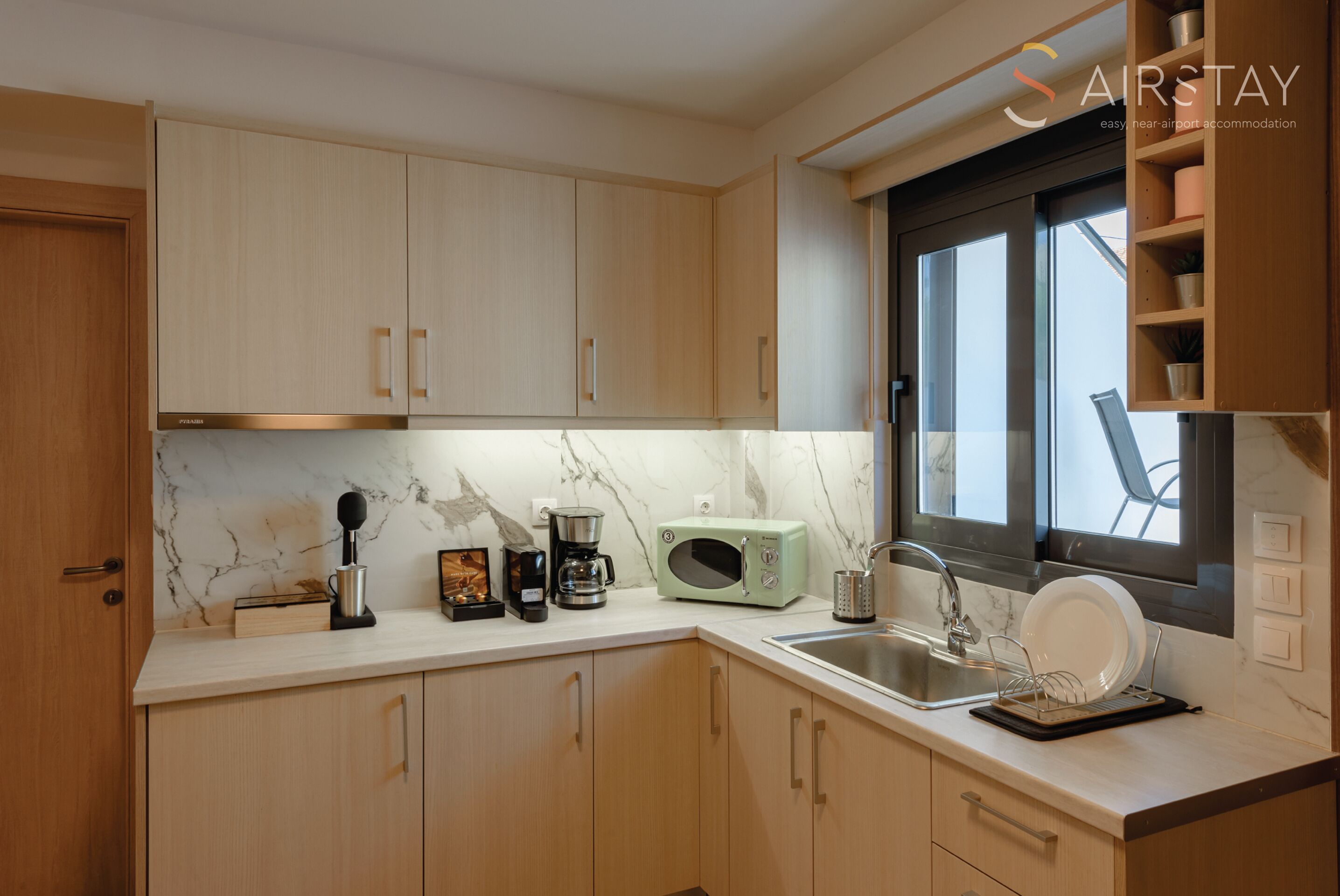 A modern kitchen with light wood cabinets, a marble backsplash, and a window with a view.