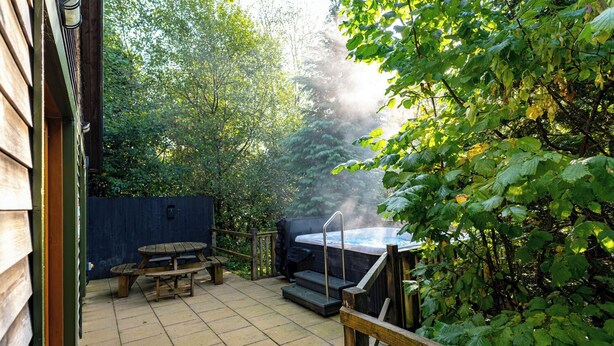 Una terraza de madera con un jacuzzi, una mesa de picnic y una valla de madera.