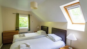 Un dormitorio con dos camas, un aparador de madera, una mesita de noche con lámpara, una ventana con vistas a zonas verdes y una luz en el techo.