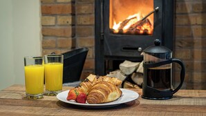 Una escena de desayuno con un plato de croissants, dos vasos de zumo de naranja y una cafetera.