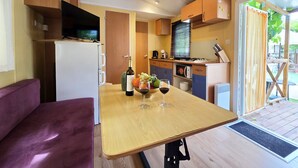 A compact kitchen with a refrigerator, stove, microwave, and wooden cabinets. - Maia: Family bungalow (Canet de Mar)