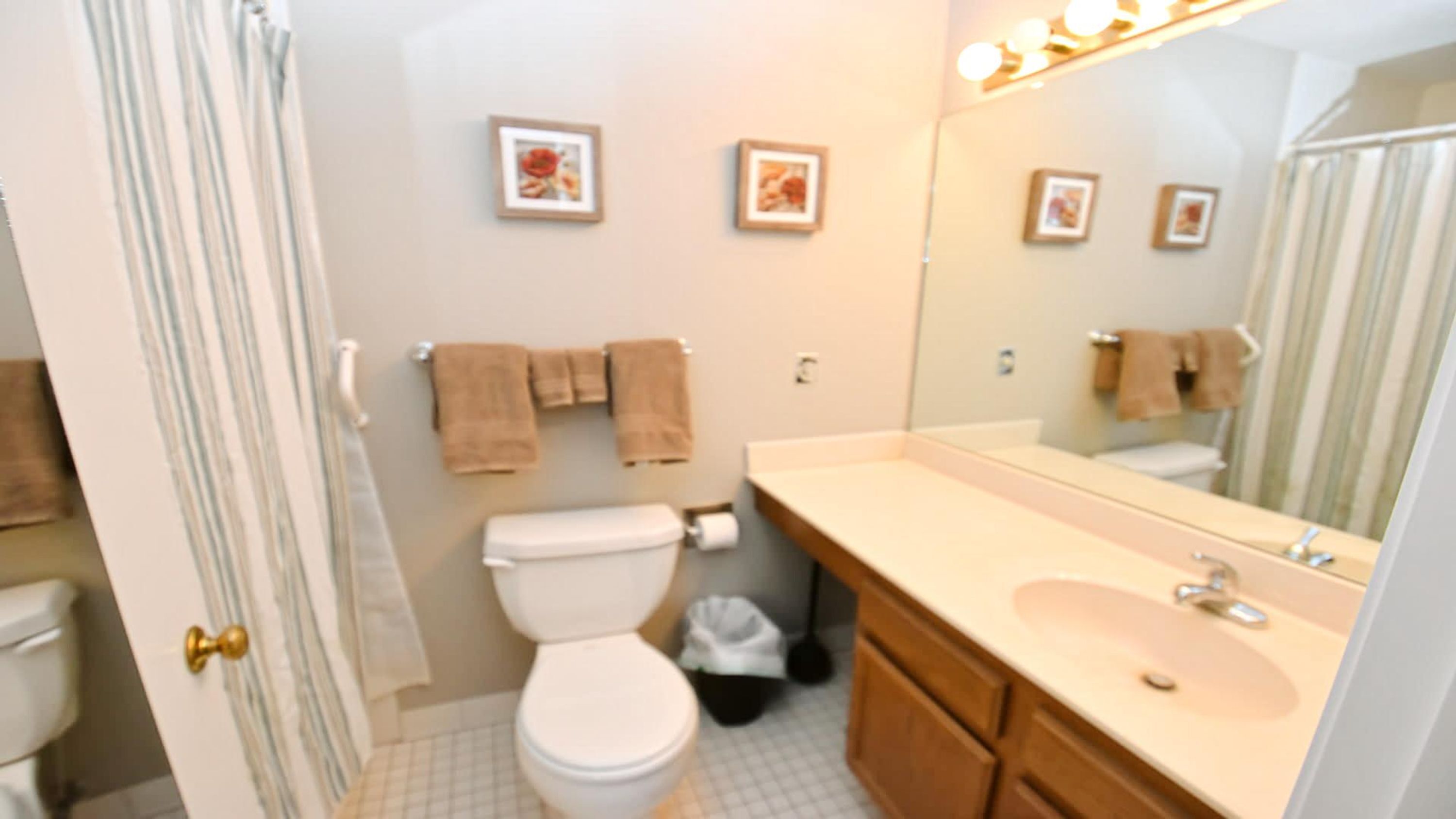 A bathroom with a toilet, sink, and mirror. There are towels hanging on the wall and a trash bin.