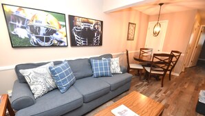 A living room with a grey sofa, wooden coffee table, and a dining area with a table and chairs. - Condo at the University of Notre Dame D3 (South Bend)