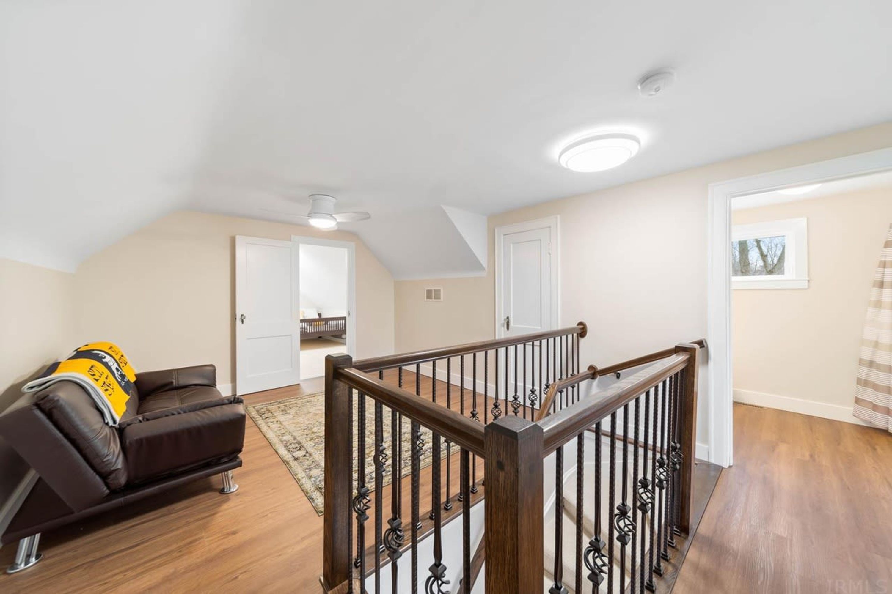 A spacious living area with a wooden staircase, a leather sofa, and a ceiling fan.