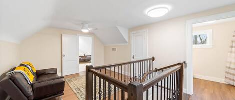 A spacious living area with a wooden staircase, a leather sofa, and a ceiling fan.