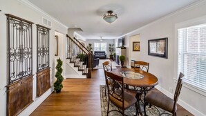 A spacious dining area with a wooden table and chairs, a staircase with wrought iron railings, and a view into the living room. - Modern Home Just 10 Mins to Notre Dame 18384 (South Bend)