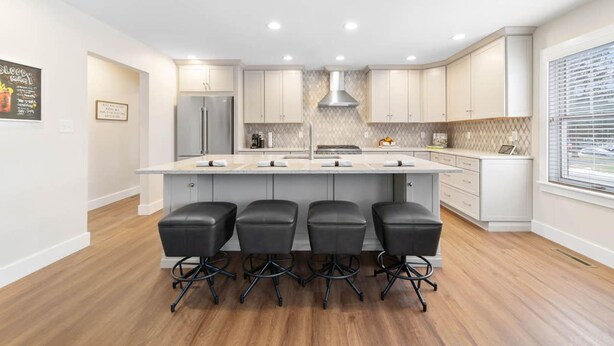 A modern kitchen with a central island, four bar stools, and a large refrigerator. - Modern Home Just 10 Mins to Notre Dame 18384 (South Bend)