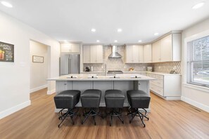 A modern kitchen with a central island, four bar stools, and a large refrigerator. - Modern Home Just 10 Mins to Notre Dame 18384 (South Bend)