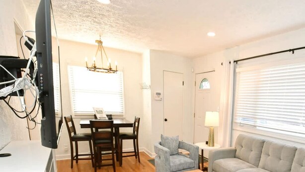 A living room with a wooden floor, a grey sofa, a small armchair, a coffee table, and a dining area with a table and chairs. - Remodeled Home 1 Mile From Notre Dame 1150 (South Bend)