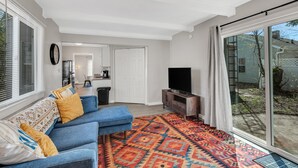 Un salon avec un canapé bleu, un tapis à motifs et un téléviseur posé sur un meuble en bois.