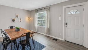 Un coin repas avec une table et des chaises en bois, une fenêtre avec des rideaux et une porte blanche dotée d’une fenêtre.