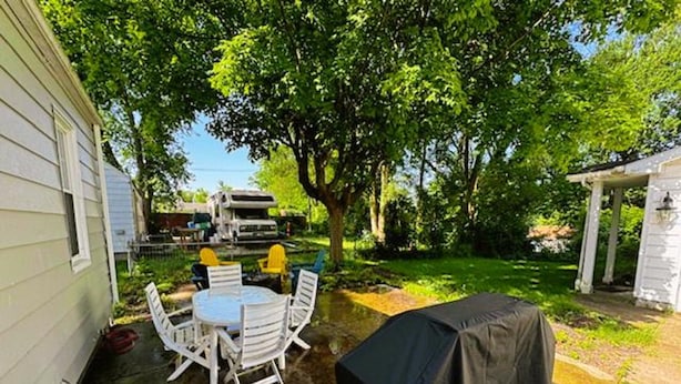 Un jardin avec un barbecue couvert, une table ronde entourée de chaises et un espace patio abrité.