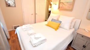 A neatly made bed with white and yellow bedding, a bedside table with a lamp, and a small cabinet. - Extra Entertainment Space Just 7 Blocks to ND Campus 54211 (Mishawaka)