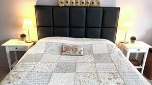 Una cama bien tendida con colcha, dos mesitas de noche con lámparas y un cabecero decorativo.