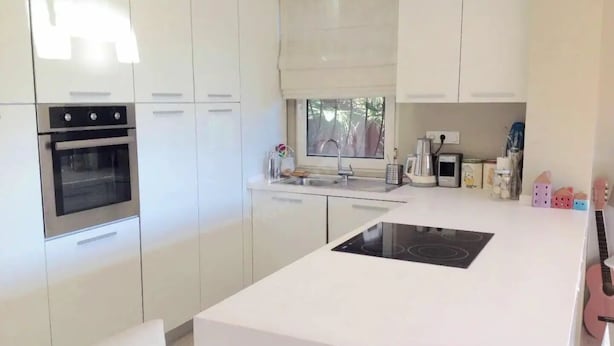 Una cocina moderna con muebles blancos, horno empotrado, placa de cocina y ventana que proporciona luz natural.