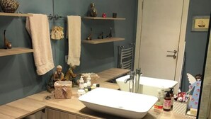 Un baño con un espejo grande, un lavamanos y estantes con toallas y artículos de aseo.