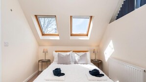 A bedroom with a large bed, two bedside tables, two lamps, and two skylights.