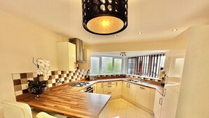 A modern kitchen with a wooden countertop, white chairs, a built-in oven, and a window providing natural light.