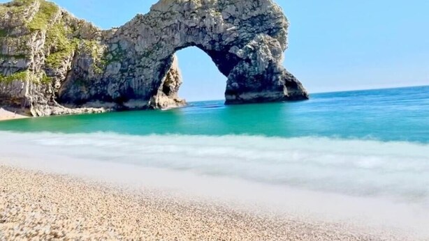 A natural rock arch formation over a beach with clear turquoise water.
