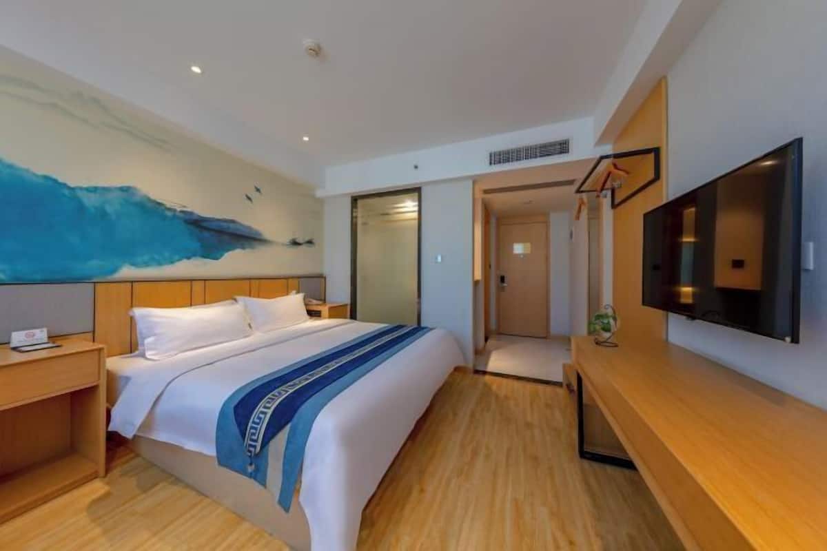 A hotel room with a large bed, a flat-screen TV, wooden flooring, and a painting on the wall.