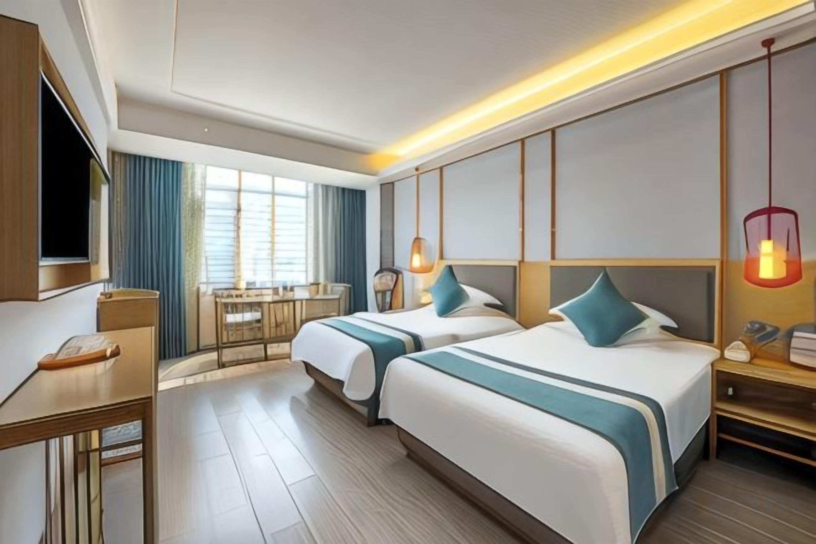 A hotel room with two beds, a desk, a TV, and a dining area.