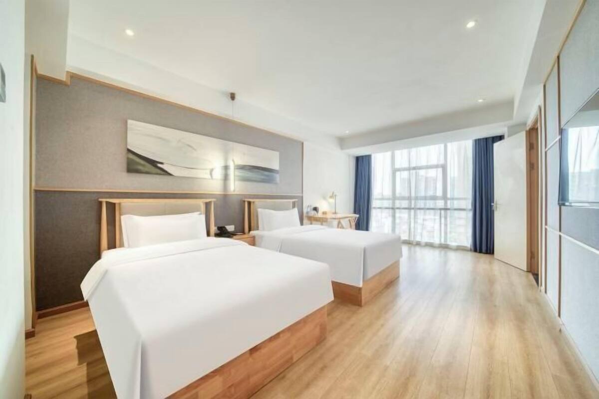 A hotel room with two beds, a large window with curtains, and a modern design.