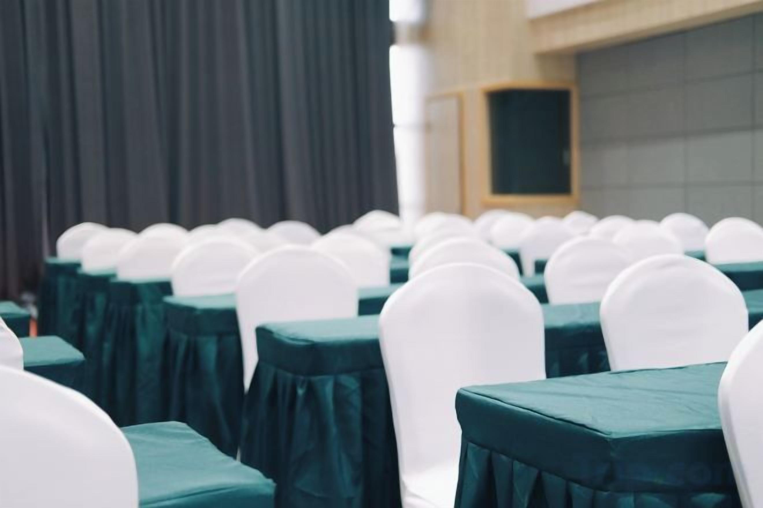 Filas de mesas con sillas blancas y manteles verdes, dispuestas en un salón de banquetes.