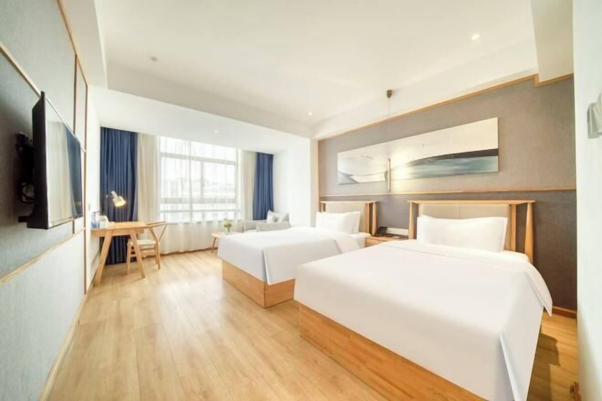 A hotel room with two beds, a desk, and a large window with curtains.
