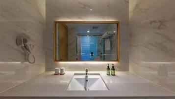 A modern bathroom with a marble wall, a large mirror, a sink, and a hairdryer on the left.