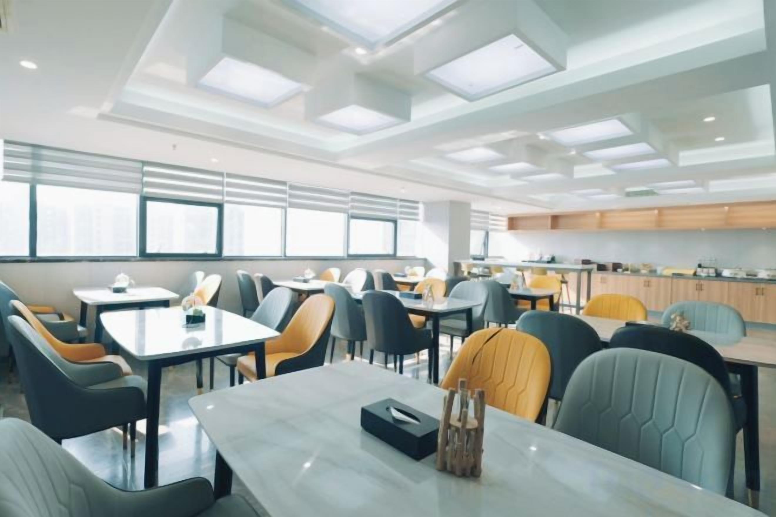 Un comedor moderno con mesas y sillas, una cocina al fondo y ventanas amplias.