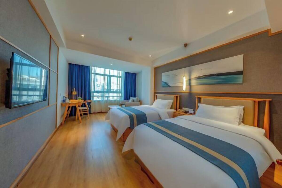 A hotel room with two beds, a desk, and a large window.