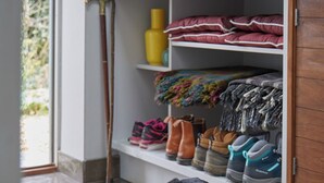A black dog lying on a white pet bed in a room with tiled flooring, a wooden cabinet, and shelves with shoes and a cane. -  Well equipped lodge,  Next to Holkham Hall and villages close to the Beach  (Holkham wells by the sea)