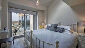 A bedroom with a large bed, a nightstand, a lamp, and a view of the outdoors through a sliding glass door. -  Well equipped lodge,  Next to Holkham Hall and villages close to the Beach  (Holkham wells by the sea)