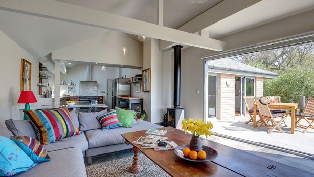 A modern living room with a grey sofa, colorful pillows, a wooden coffee table with newspapers, and a vase with flowers. -  Well equipped lodge,  Next to Holkham Hall and villages close to the Beach  (Holkham wells by the sea)